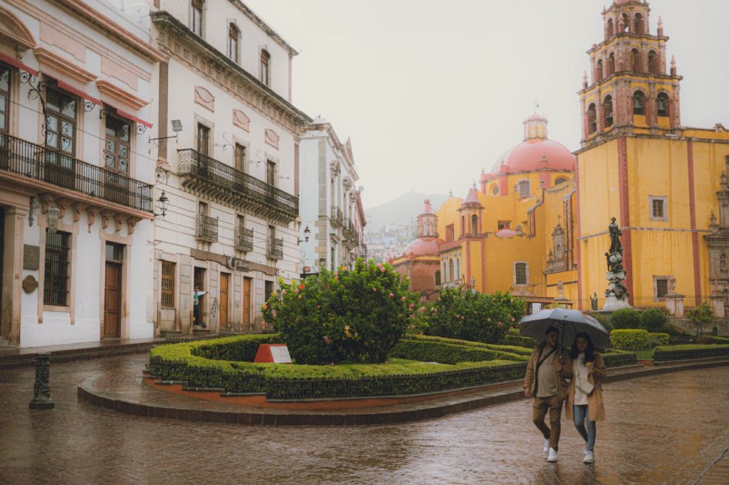 pexels-photo-32694771 Couple walking under umbrella near Basílica de Nuestra Señora in rainy Guanajuato, Mexico.